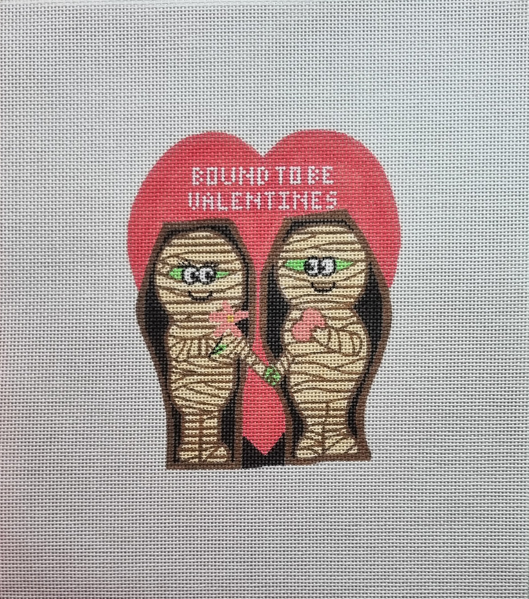Needlepoint design of two mummies holding a heart with 'Evident to be VALENTINES' text on a gray fabric background.